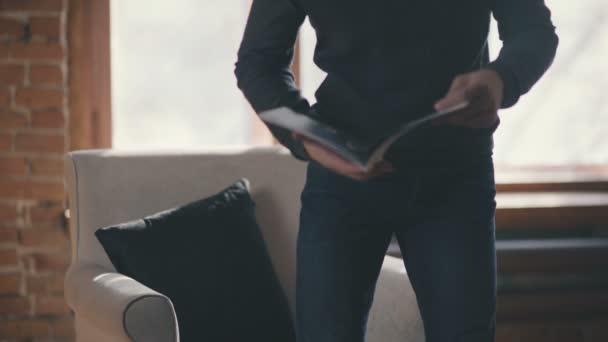 Middelbare leeftijd man met bril en een baard zit in een fauteuil met boek — Stockvideo