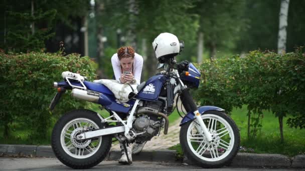 Novosibirsk 2016: Vrouw leunde ellebogen op een motorfiets en het typen van sms — Stockvideo