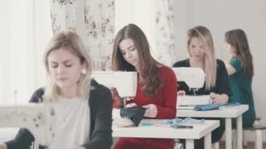 Kızlar seamstresses birbiri ardına oturmak ve dikiş makineleri üzerinde dikmek.