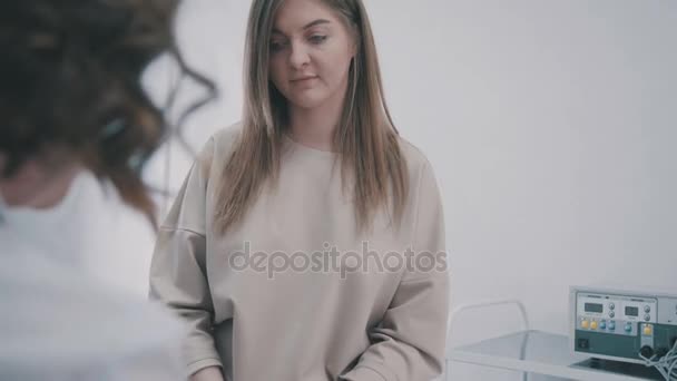 En ung kvinna i receptionen på en läkare lyssnar till terapeuten — Stockvideo