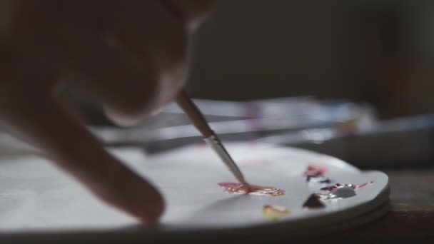 Artista tampona pennello in una tavolozza con vernici e applica striscio su tela — Video Stock
