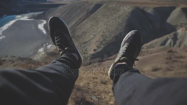 Turystyczna siedzi na skraju góry klif i szczękając z jego stóp — Wideo stockowe