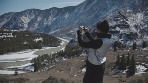 Юная леди-туристка стоит на вершине горы и фотографирует — стоковое видео