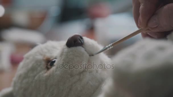 Proceso de creación de un osito de peluche: el maestro pinta una bonita sonrisa de juguete . — Vídeo de stock