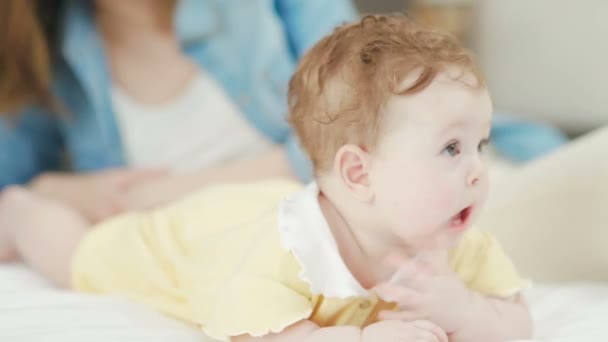 Bebê menina encontra-se em seu estômago na cama, mamãe beija sua filha . — Vídeo de Stock
