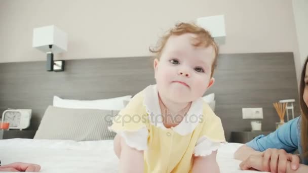 En rolig liten flicka försöker krypa på sängen och ser sig omkring. — Stockvideo