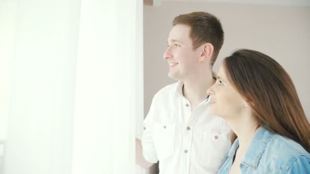 Una pareja feliz y enamorada está de pie junto a la ventana con cortinas . — Vídeo de stock