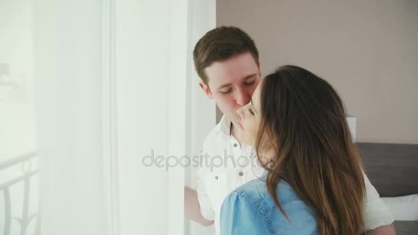 Мужчина и женщина стоят перед окном, он целует ее. . — стоковое видео