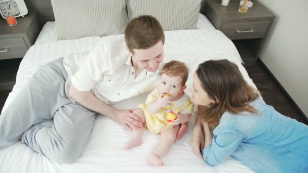 Vista superior: familia joven y feliz con un bebé en la cama juntos . — Vídeo de stock