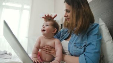 Bir dizüstü bilgisayar ile modern bir anne bebeğine dokunur. Mutlu anne
