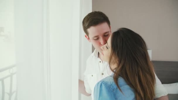 A man and a woman are standing in front of the window, he kisses her. — Stock Video