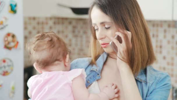 Mamma sta tenendo il suo bambino tra le braccia mentre parla al telefono . — Video Stock