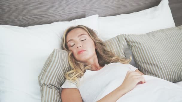 En söt blondin sover på en ljus säng. Tidigare morgon — Stockvideo