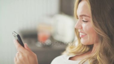 Güzel bir kadın bir smartphone kullanarak bir ileti yazarak bir ışık yatakta.