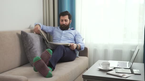 Homem no casual shitr e engraçado brilhante meias em um sofá com jornal — Vídeo de Stock
