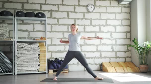 Middle-aged woman does yoga in a bright space with a brick wall — Stock Video