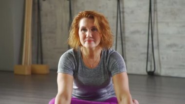 Olgun bir kadın kamera seyir Yoga asanas gerçekleştirir.