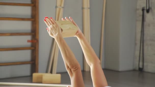 Uma mulher praticando ioga, usando um cubo de madeira - um bloco para ioga . — Vídeo de Stock