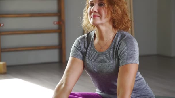Жінка сидить на килимку для йоги і змінює асан . — стокове відео