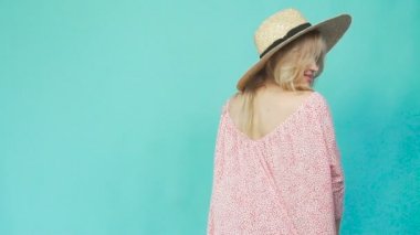 Bir kız bir hasır şapka ve bir yazlık elbise döner ve bir elbise gösterir.