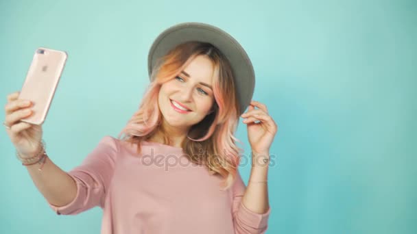 Chica en vestido rosa y sombrero hacen selfie sobre un fondo turquesa — Vídeo de stock