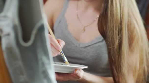 Девушка-художник в серой рубашке смешивает цвета в палитре, готовится к рисованию — стоковое видео