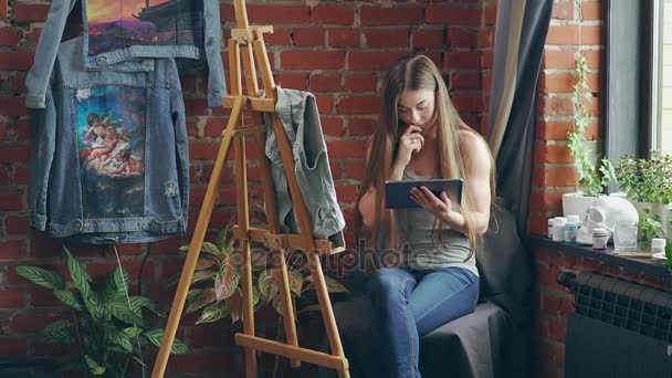 Vrouwelijke kunstenaar in de buurt van een ezel met een tablet op zoek naar een patroon — Stockvideo