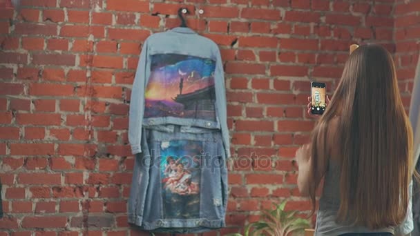 Довге волосся дівчина стоїть навпроти стіни і робить фотографію для продажу — стокове відео