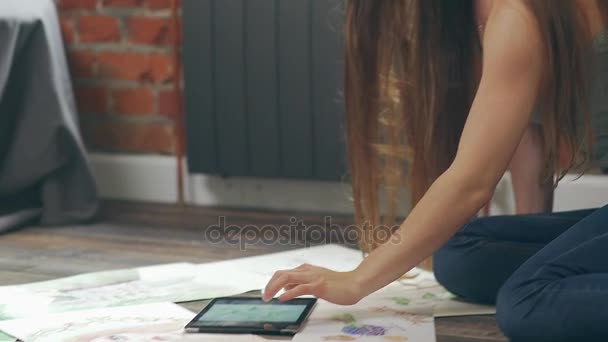 Жінка-художник на підлозі дивиться на фотографії, вибирає візерунки з вкладкою — стокове відео