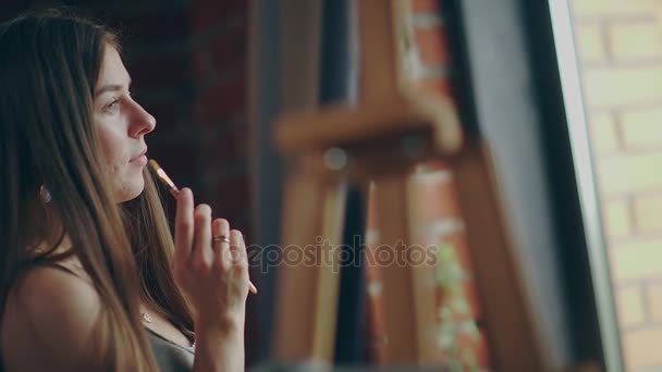 Profile of the young artist: she stands by the window, holds the brush — Stock Video