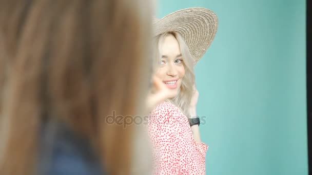 Ein hübsches Mädchen mit Hut auf türkisfarbenem Hintergrund, sie wird fotografiert. — Stockvideo
