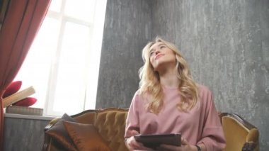 Kadın gülümsüyor ve elinde bir tablet ile bir odada otururken rüyalar