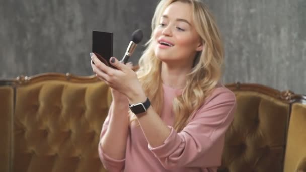 Beautiful blonde correct makeup and applies a blush, using a brush — Stock Video
