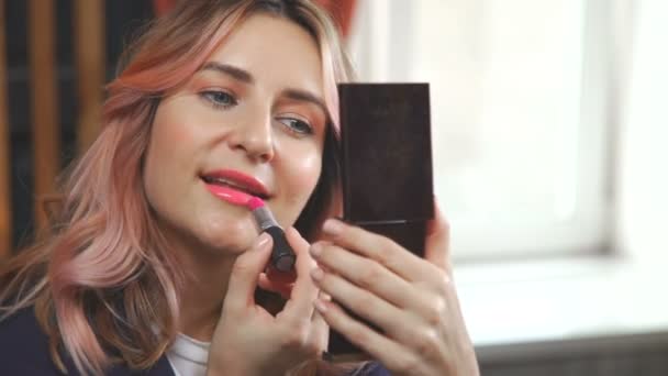 Jonge vrouw bekijkt zichzelf in de spiegel van een zak en make-up past — Stockvideo