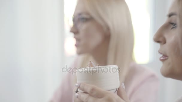 Молодая женщина с острыми чертами лица пьет чай и смотрит на сострадающих — стоковое видео