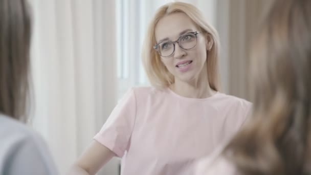 Femme blonde avec des lunettes boit du thé et parle avec des copines dans le café — Video