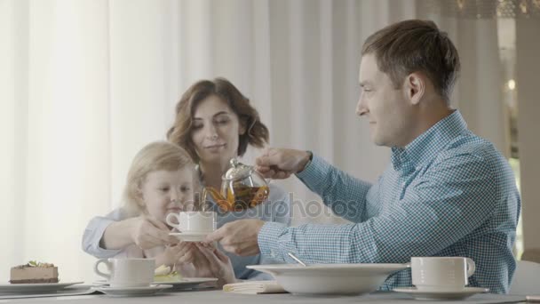 Ojciec wlewa herbatę w biały kubek dla żony i córki. — Wideo stockowe