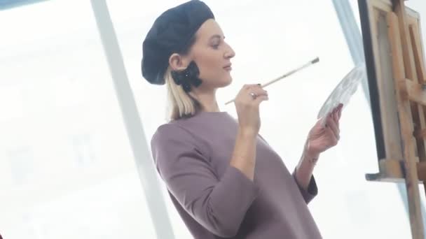 Künstlerin mit Baskenmütze, Pinsel und Zeichnung in der Hand, lächelnd — Stockvideo