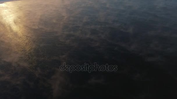 Vuela sobre la superficie del agua: el agua oscura se congela, el atardecer se refleja — Vídeo de stock