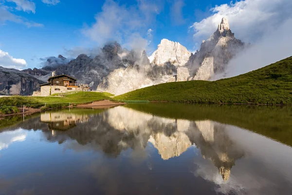 Los picos de Pale di San Martino (Dolomitas italianas) reflejados en el agua, con un chalet alpino sobre fondo . — Foto de Stock
