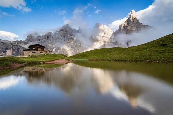 De toppen van de Pale di San Martino (Italiaanse Dolomieten) weerspiegeld in het water, met een alpine chalet op achtergrond. — Stockfoto