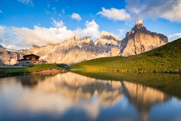 Пики Бледного Сан-Мартино (итальянские Доломиты) отражаются в воде на закате, на фоне альпийского шале
.