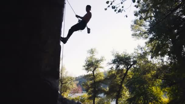 Silueta del hombre escalando en la roca acantilado de la parte inferior — Vídeo de stock