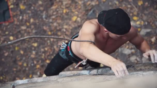 Junger Mann mit Mütze klettert den Felsen hinauf — Stockvideo