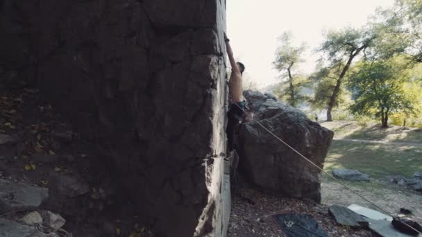 Человек в шапке спускается по скале на веревке — стоковое видео