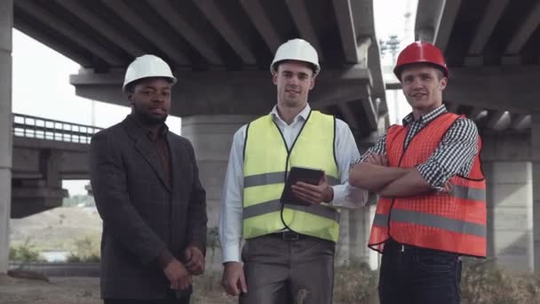 Drie architecten in beschermende helmen kijken camera — Stockvideo