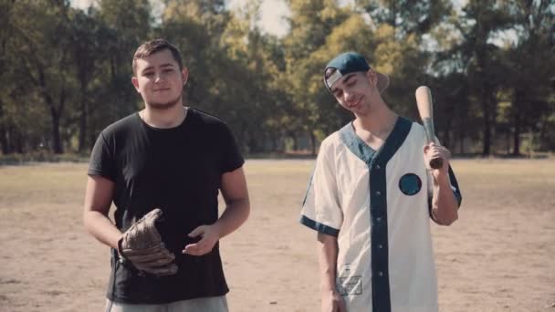 Två unga män på väg att spela baseball i parken — Stockvideo