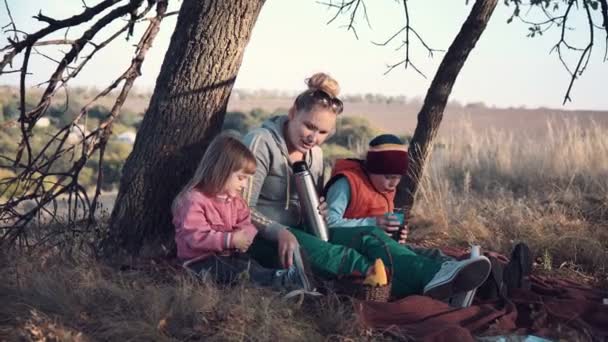 Mutter und Kinder genießen warmes Getränk unter Baum — Stockvideo