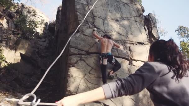 Man climbing the cliff with woman belaying him — Stockvideo