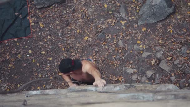 Молодой человек в кепке взбирается на скалу — стоковое видео